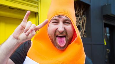 A man in fancy dress sticks out his tongue and makes a 'rock metal' gesture with his hands 