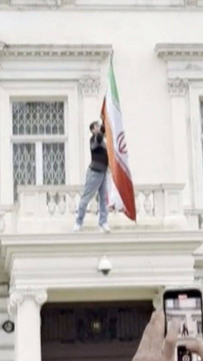 A protester is on the balcony of the Iranian embassy, tearing down a flag