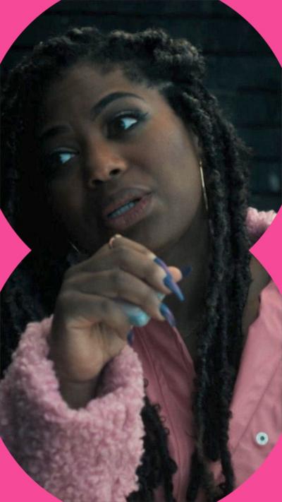 Sharla is speaking, her hand is partly in front of her face, she is wearing a pink coat