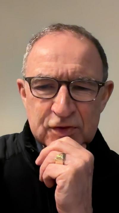 Man with short grey hair and glasses with his hand on his chin, he is wearing a gold wedding ring.