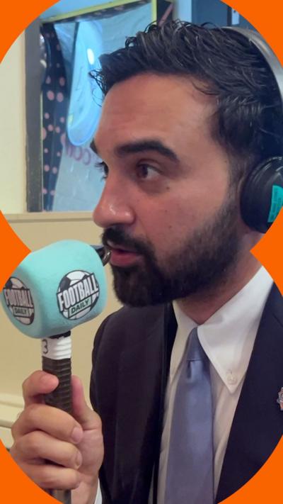 A man with short dark hair and a short dark beard talks into a microphone
