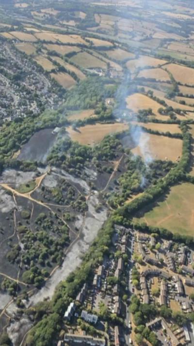 A drone footage of fields. There is smoke coming from the field.