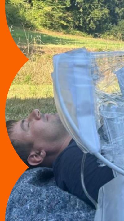 A person lying down in a grassy field demonstrating how to use a portable operating theatre called SurgiBox