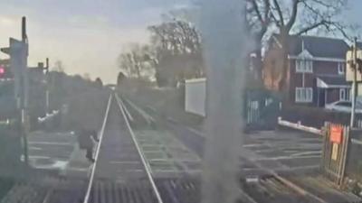 Woman steps out and then can be seen tilting back off the tracks as a train comes