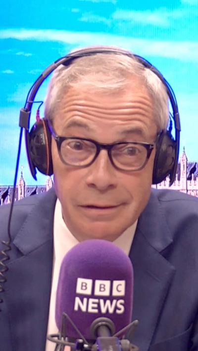 Nigel Farage wearing headphones and a suit sits in front of a purple BBC microphone.