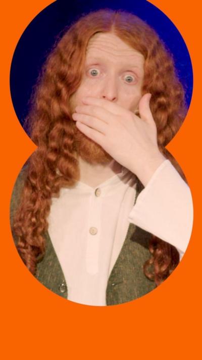 A man with long red hair and a green waistcoat clasps mouth over hands in shock.