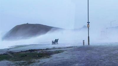 Waves crash onto a road in Troon, with water sweeping over a bench