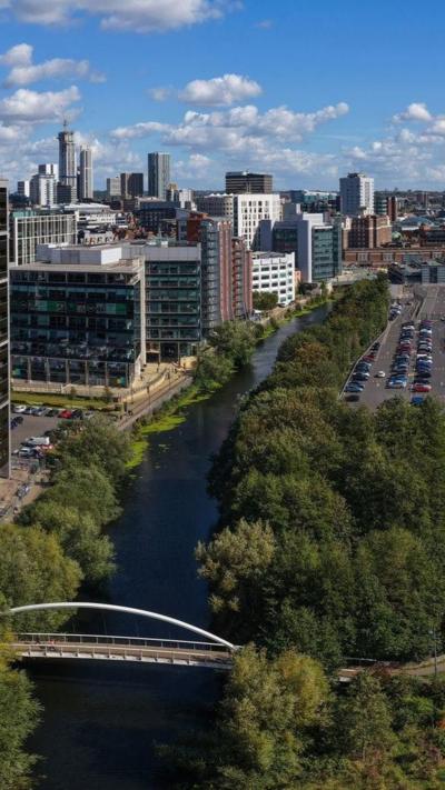 Aerial panorama of Leeds city centre skyline with River Aire, modern high-rises, and railway tracks in Yorkshire, England.