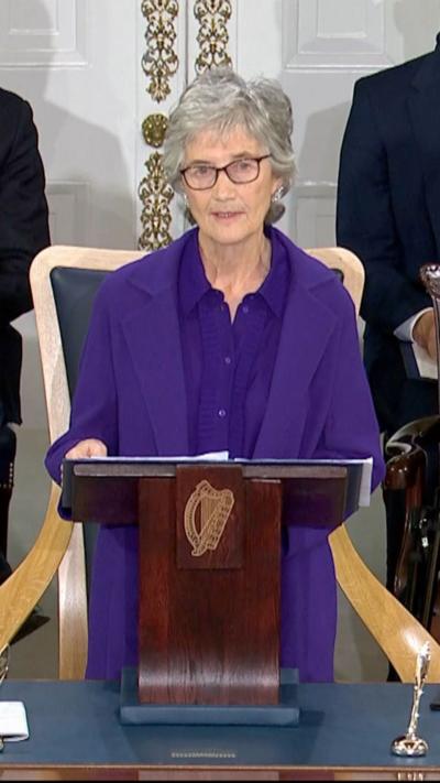 Catherine Connolly is wearing a purple suit and is speaking at a stand