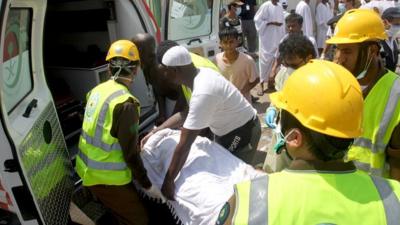 Saudi emergency personnel and Hajj pilgrims load a wounded person into an ambulance