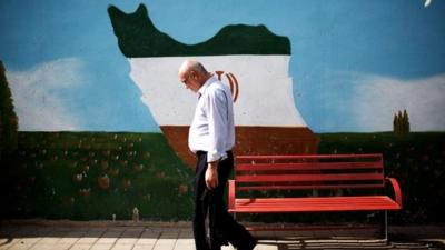 An Iranian man walks past a mural displaying the Iranian map