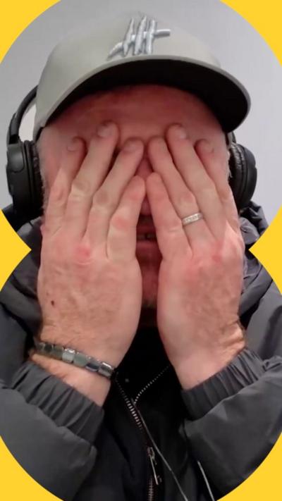 Wayne Rooney is wearing a cap and has his hands over his face.