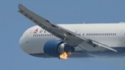 A Delta Airlines plane in the sky, with the left engine on fire.