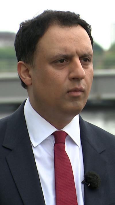 Anas Sarwar - man wearing dark suit and red tie, standing on the banks of the River Clyde