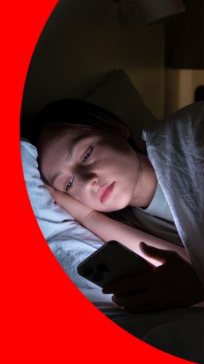 A woman lies in bed looking at her phone