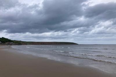 Dark storm clouds over a quiet beach, with gentle waves and distant cliffs along the coastline in Filey, North Yorkshire
