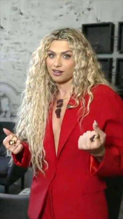 Woman with blonde curly hair looking at the camera wearing a red blazer
