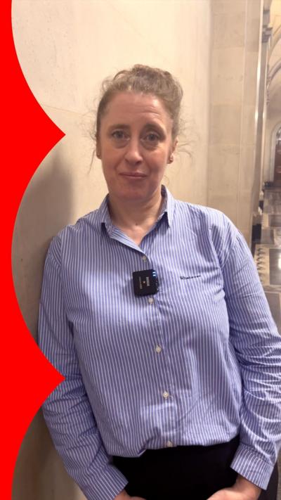 A woman in a blue striped shirt stands in a corridor 