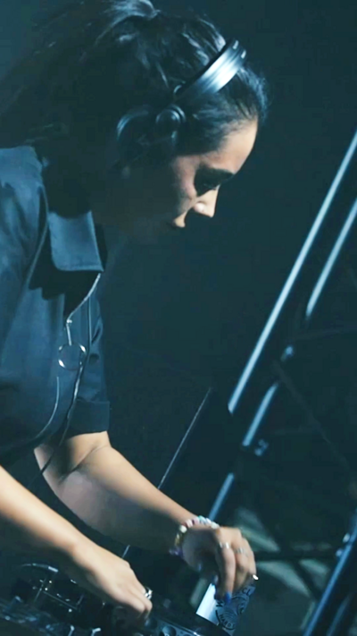 Hannah Laing in a DJ box, she has dark hair and is wearing headphones.
