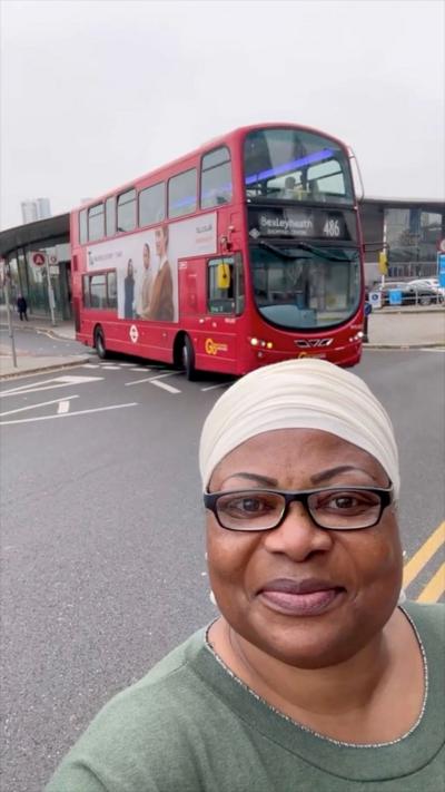 Bemi Orojuogun smiling as she wears glasses and a head covering. She is posing with a red bus behind her.