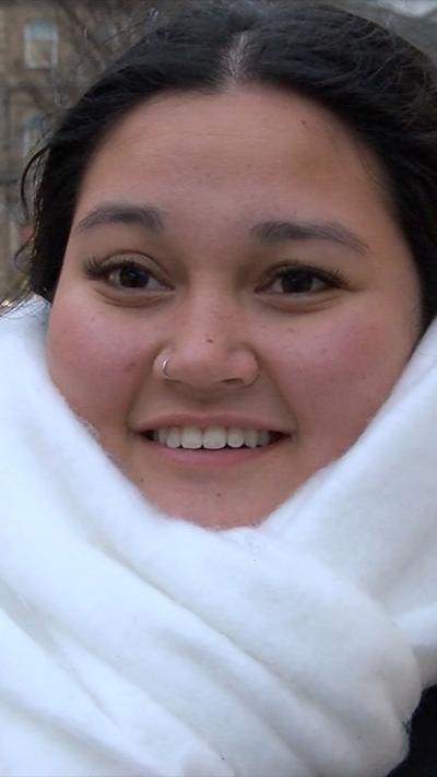 A woman with dark hair and a silver nose ring. She is wearing a large white scarf