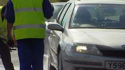 A car being stopped by a man in a high-vis vest.