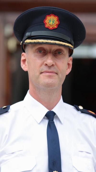 Garda commissioner in a black officer hat, white shirt and black tie. 