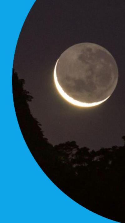 A thin crescent Moon with the darker whole visible, low on the horizon
