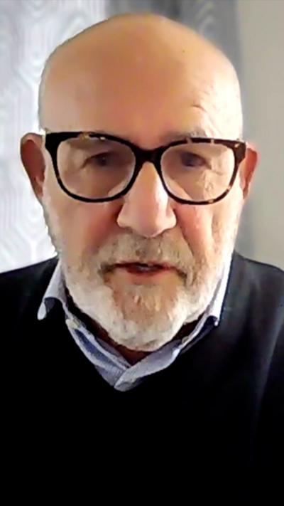 A bald man with glasses and a trimmed beard speaks into a camera