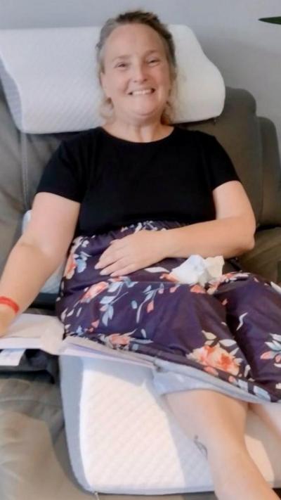 Woman sits on sofa smiling.