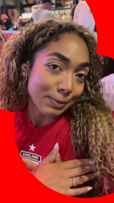 A woman wearing a red England top looks at the camera