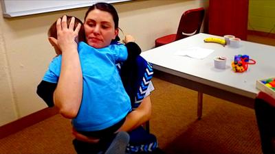 A woman hugs a child next to a table with toys on it