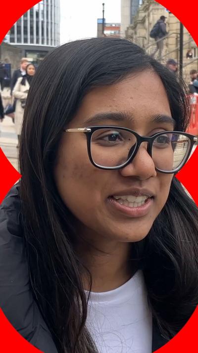 A woman with long dark hair looks offscreen. She is wear black-rimmed glasses and a white T-shirt.
