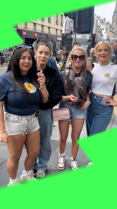 Four smiling women wear Scotland tops in an Edinburgh street