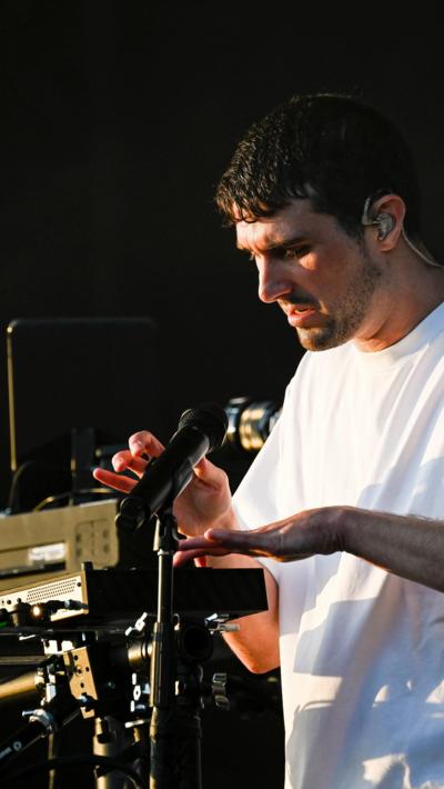 Fred Again looks sweaty and wears a white tshirt while playing an MPC as he performs at Glastonbury 2023