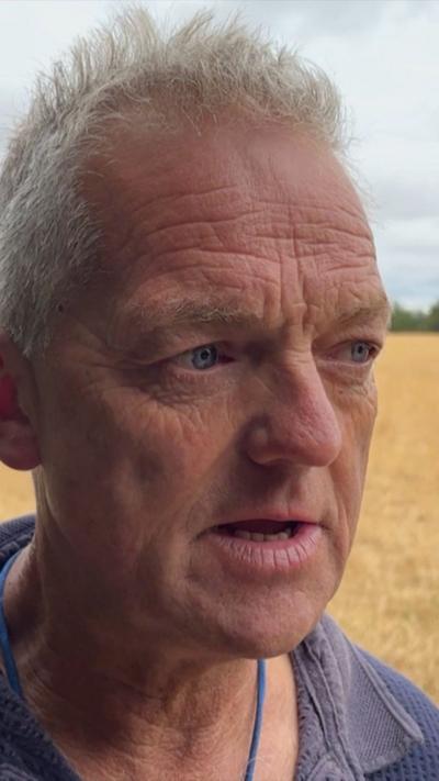 Man's head. He is standing in a ploughed field.