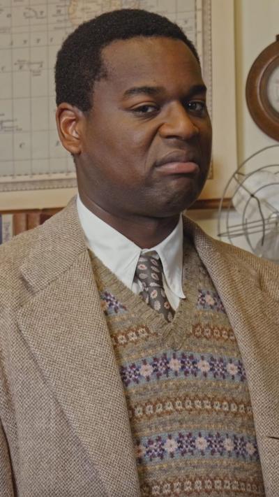 A man scowls, he is wearing a nice suit and tie and in a classroom, Mr Parker from Malory Towers.