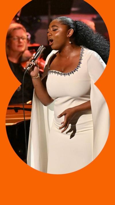 Samara Joy, wearing white and singing into a microphone, on stage at the Proms with musicians around her.