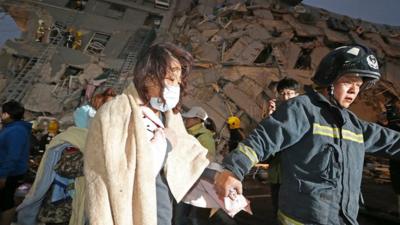 A woman is led by a rescue worker from the site of a toppled building after an earthquake in Tainan, Taiwan