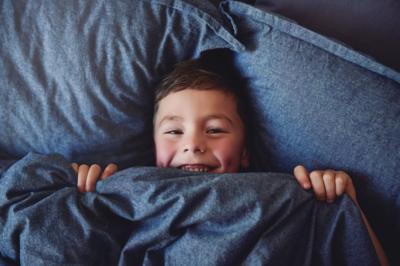 a boy smiling while lying on pillows pulling up a duvet up to his chin