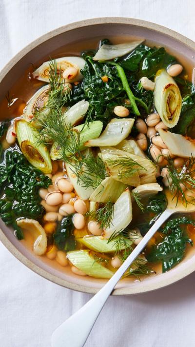 Top down image of a bowl with vegetable broth in. A spoon is in the bowl. Bread sits on a side dish next to it.