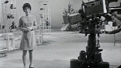 Valerie Singleton standing in front of a camera in the Blue Peter studio.