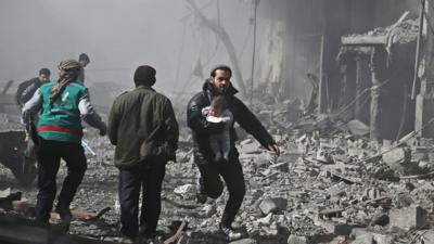 Syrian man carries an infant injured in government bombing in the besieged Eastern Ghouta region of Damascus