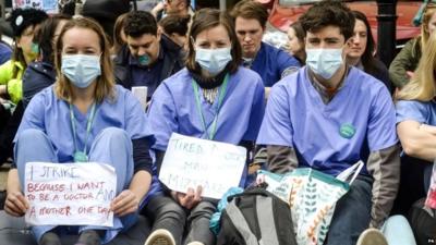 Junior doctors wear scrubs and masks as they sit down in a silent protest outside Bristol Royal Infirmary