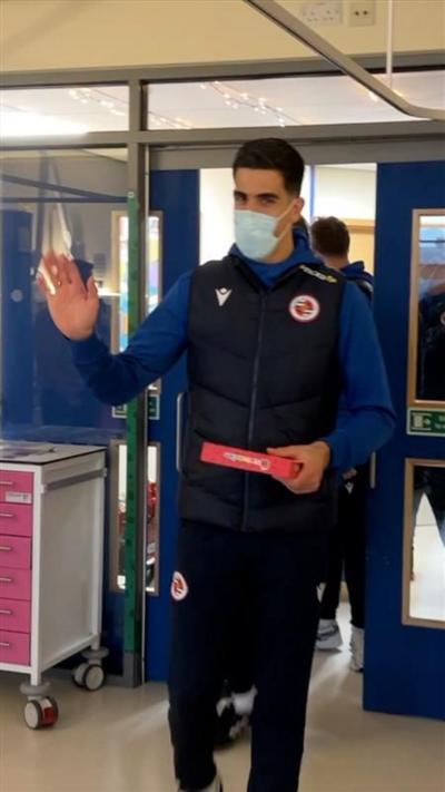 Reading football player walking into children's ward holding a gift and waving.