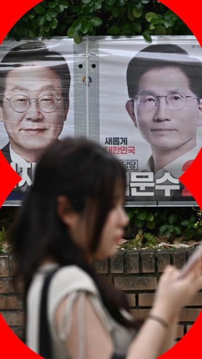 A woman walks past two posters of the South Korean election candidates Lee Jae-myung and  Kim Moon-soo
