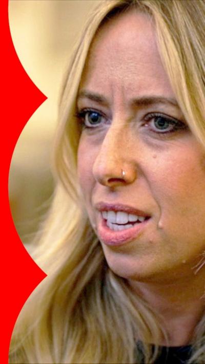 A woman with long blonde hair wearing a grey jacket looks puzzled.