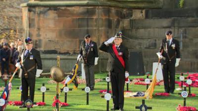 Veterans during Edinburgh's Armistice Day event. One of them is saluting while the other have heads bowed while holding flags downward. 