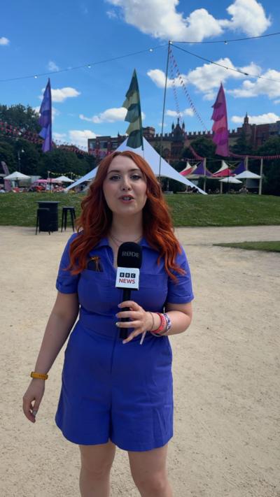 A woman in a blue dress with red hair standing in a sunny festival arena.