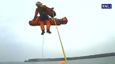 A rescuer pulls up the fisherman on a winch